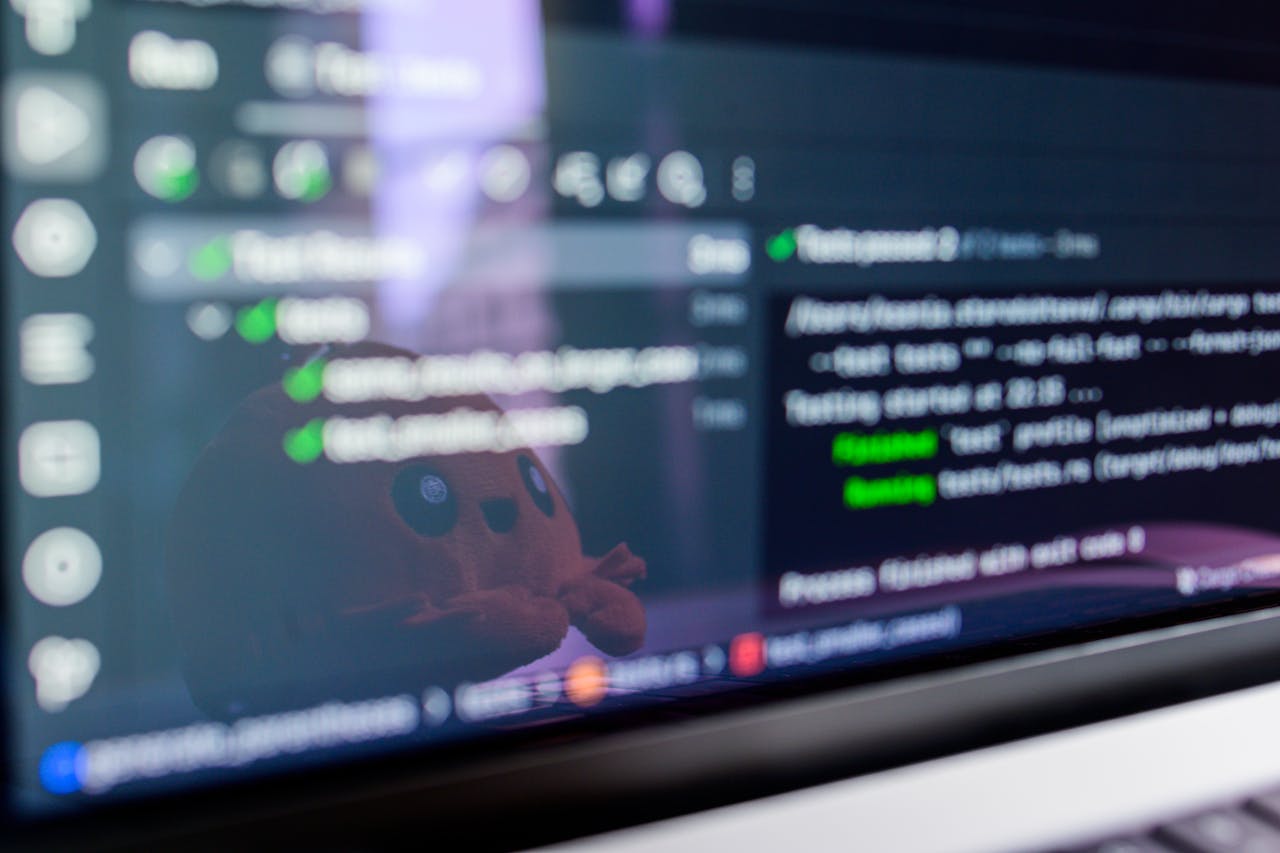 Close-up of a laptop screen displaying programming code with a cute plush toy reflecting.